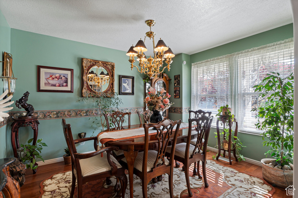 Dining area with a chandelier, wood finished floors, a textured ceiling, and baseboards