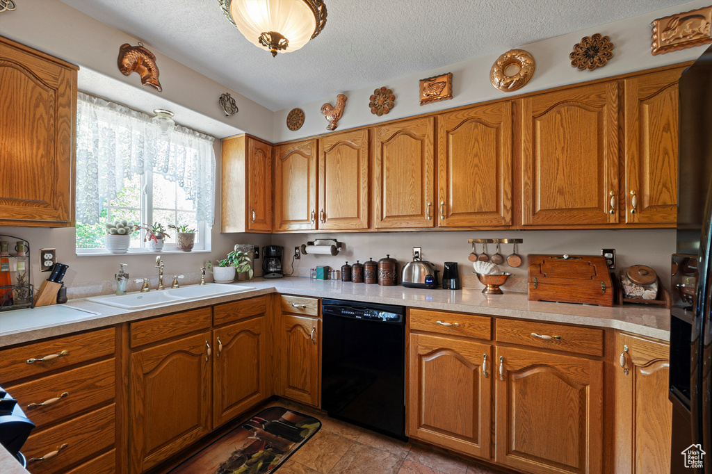 Kitchen featuring black dishwasher, a sink, brown cabinets, light countertops, and a textured ceiling