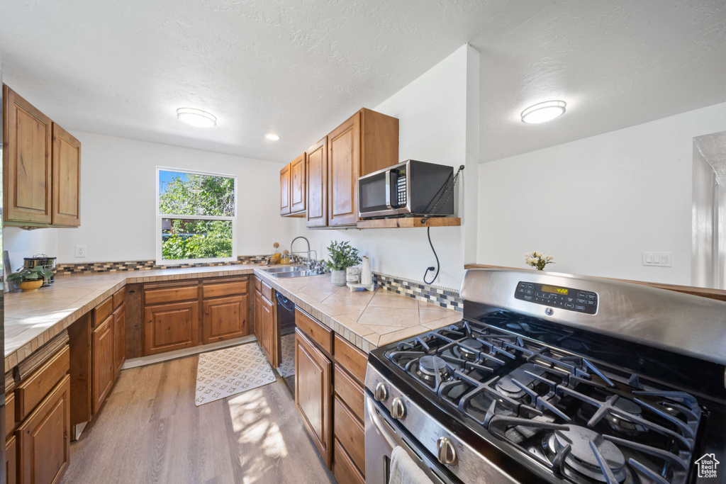 Kitchen with stainless steel appliances, a sink, light wood-style flooring, and brown cabinetry