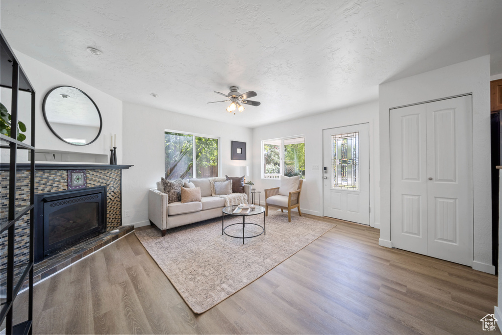 Living area with a tile fireplace, wood finished floors, ceiling fan, baseboards, and a textured ceiling
