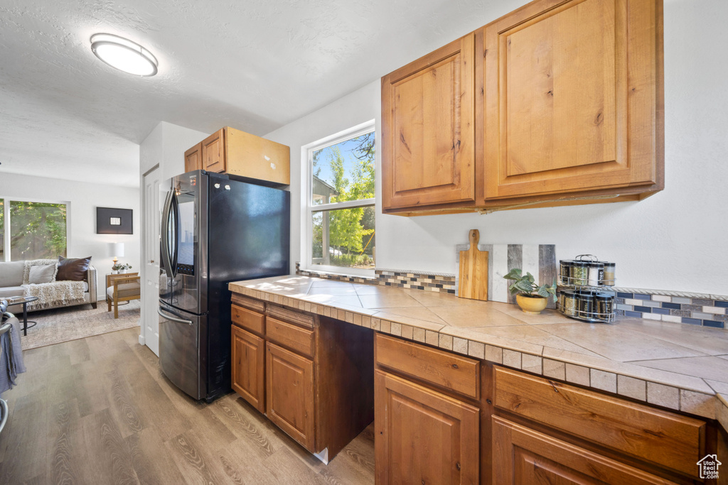 Kitchen with freestanding refrigerator, light wood-style floors, tile counters, open floor plan, and brown cabinets