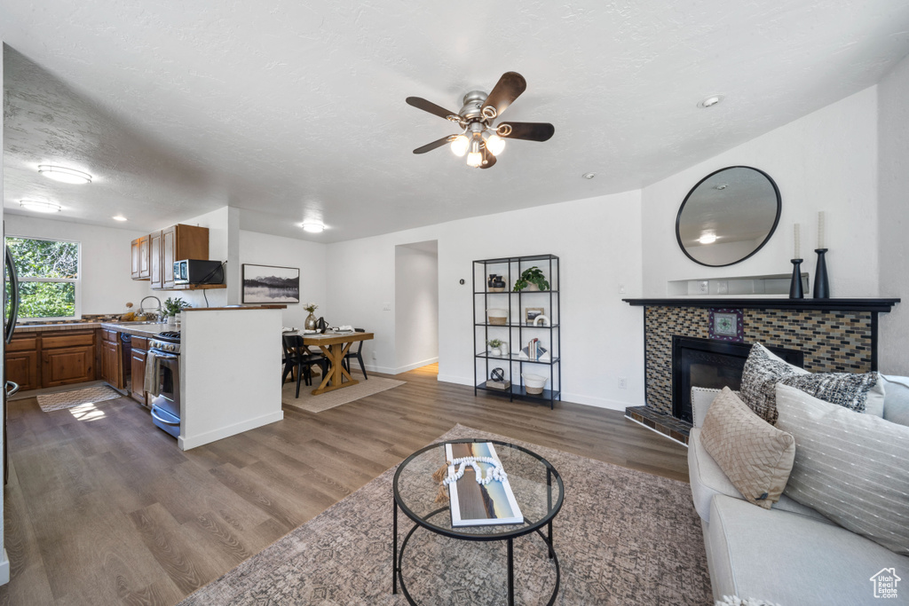 Living area with dark wood-style flooring, a tiled fireplace, a ceiling fan, and baseboards