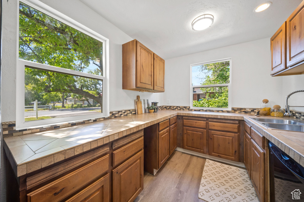 Kitchen featuring a sink, dishwasher, light wood-style flooring, brown cabinets, and tile counters