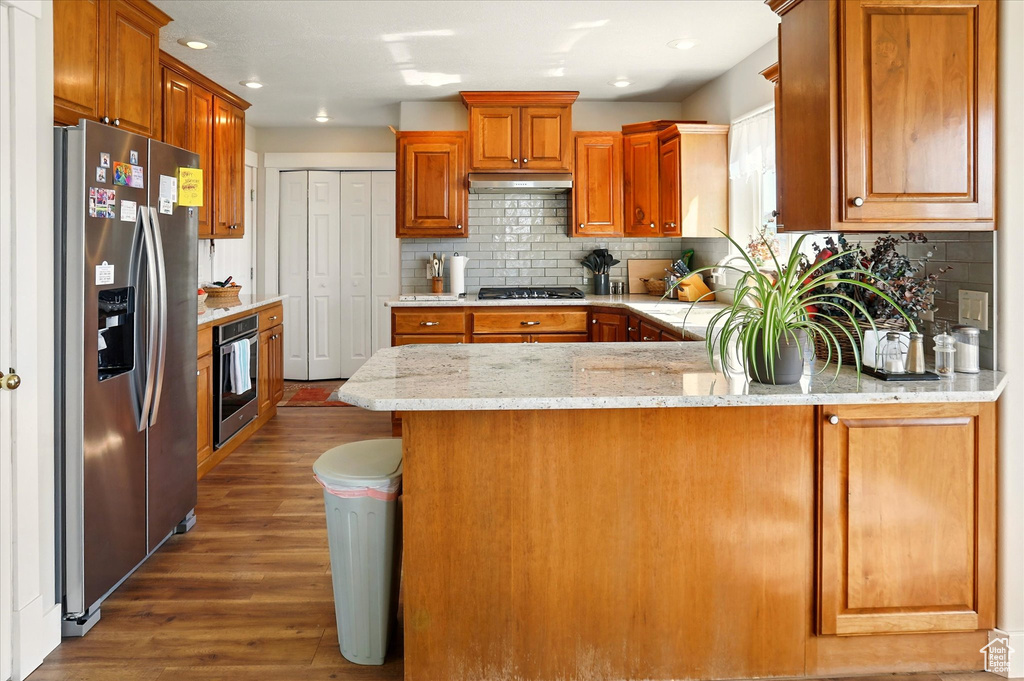 Kitchen featuring appliances with stainless steel finishes, wood finished floors, tasteful backsplash, a peninsula, and recessed lighting