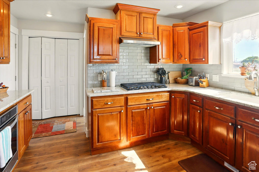Kitchen featuring under cabinet range hood, appliances with stainless steel finishes, a sink, dark wood-style floors, and light stone countertops