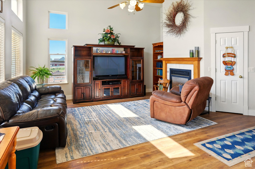 Living room featuring ceiling fan, wood finished floors, a high ceiling, and a fireplace