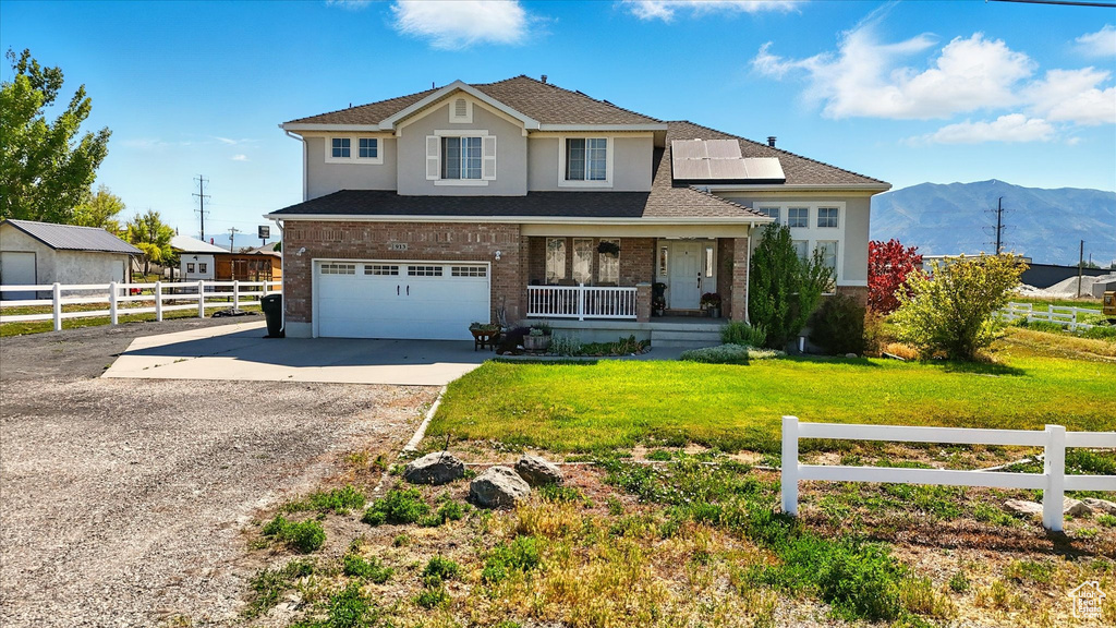 Traditional home with a porch, concrete driveway, solar panels, an attached garage, and a mountain view