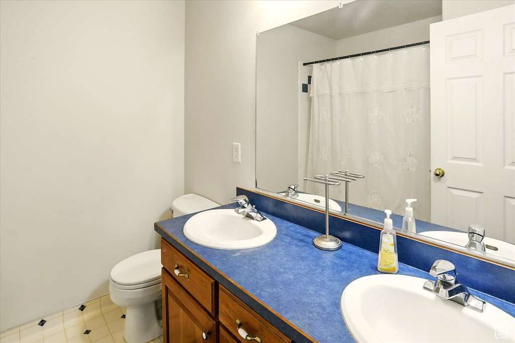 Full bathroom with toilet, double vanity, tile patterned floors, and baseboards