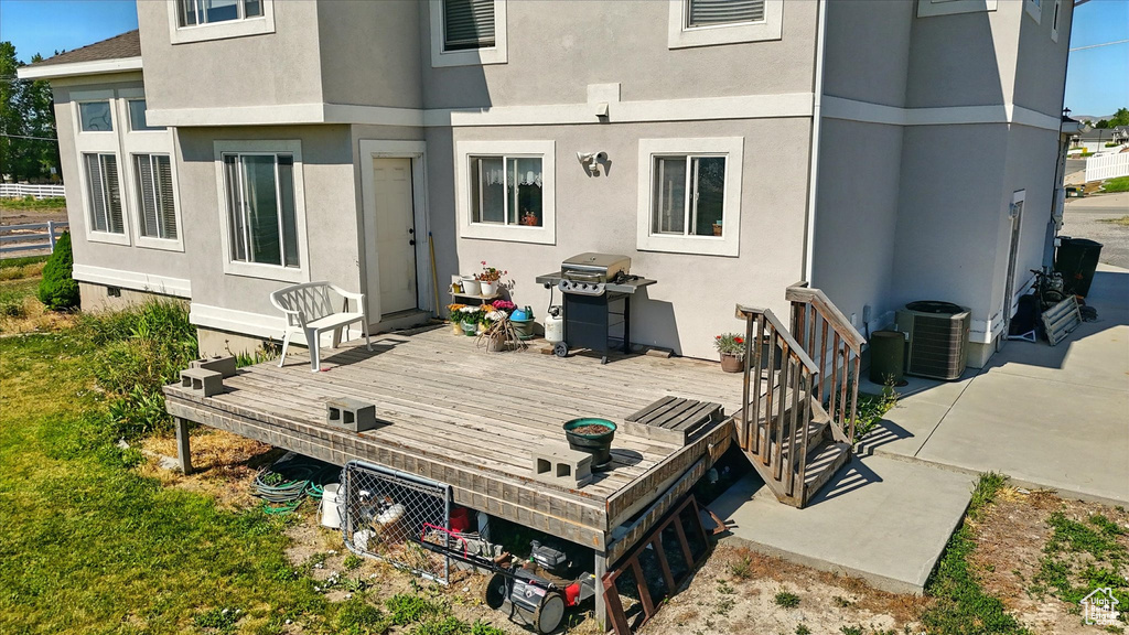 Rear view of property with a wooden deck, stucco siding, and central AC