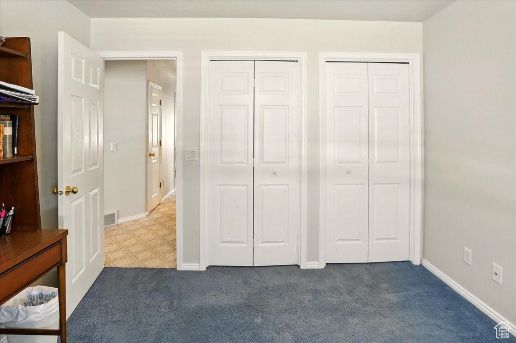 Unfurnished bedroom with multiple closets, dark colored carpet, and baseboards