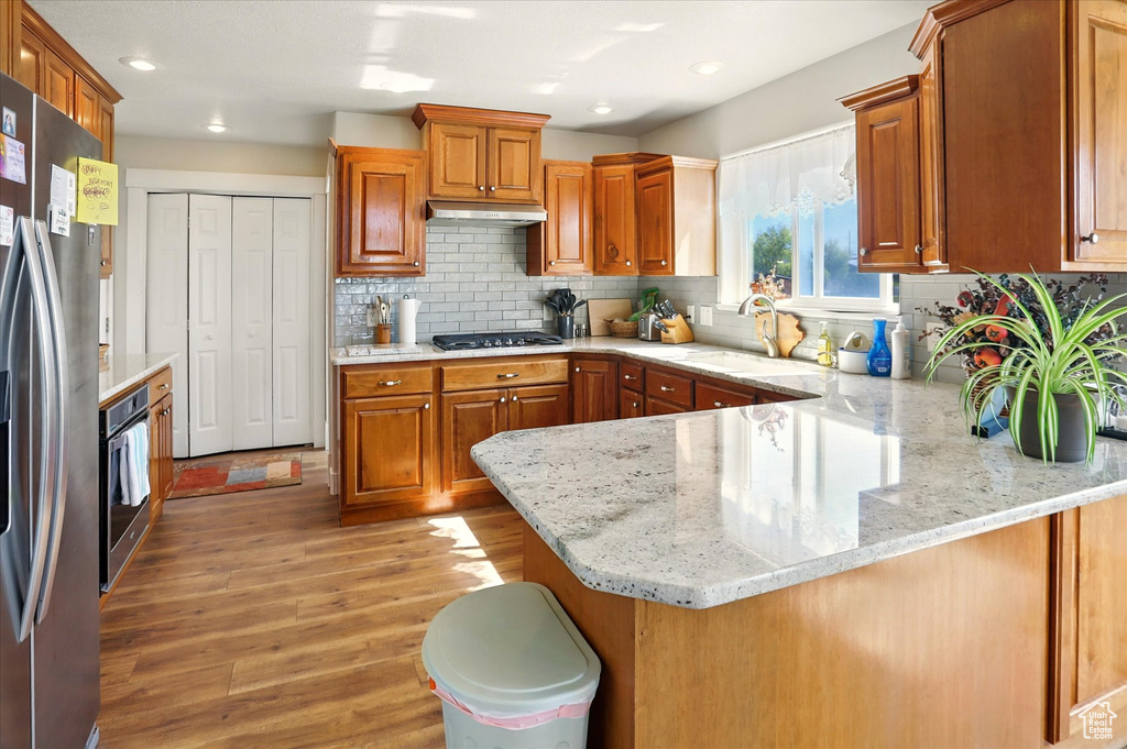 Kitchen featuring a sink, stainless steel appliances, under cabinet range hood, a peninsula, and light wood-style flooring