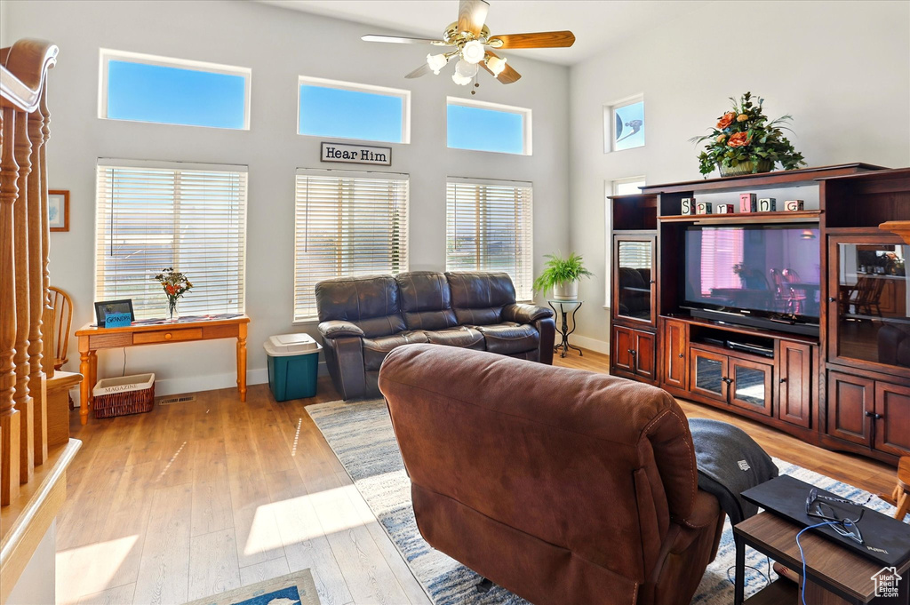 Living room with ceiling fan, light wood finished floors, a towering ceiling, and baseboards