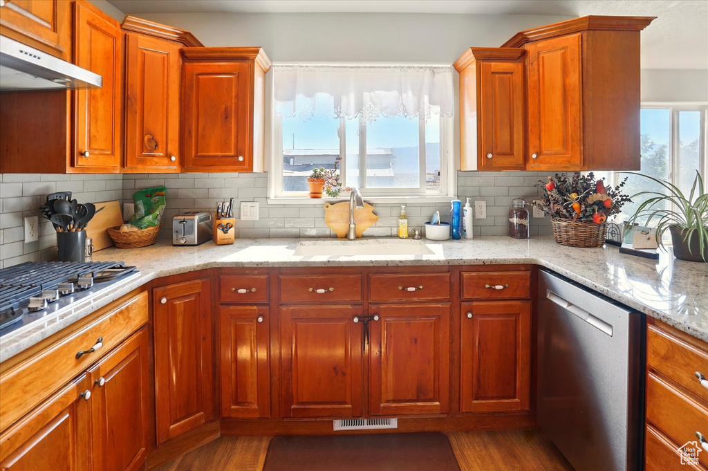 Kitchen with stainless steel appliances, under cabinet range hood, a sink, dark wood-style flooring, and decorative backsplash