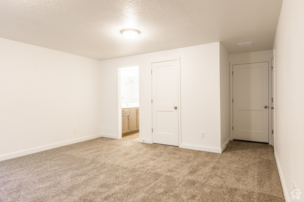 Unfurnished bedroom featuring light carpet, ensuite bath, and a textured ceiling