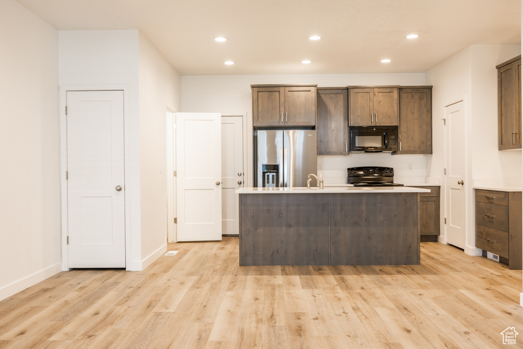 Kitchen with light wood-type flooring, sink, an island with sink, and black appliances
