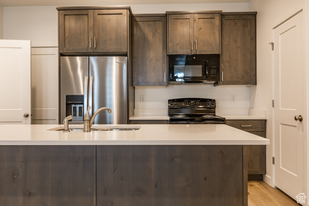 Kitchen with dark brown cabinetry, light hardwood / wood-style floors, sink, and black appliances