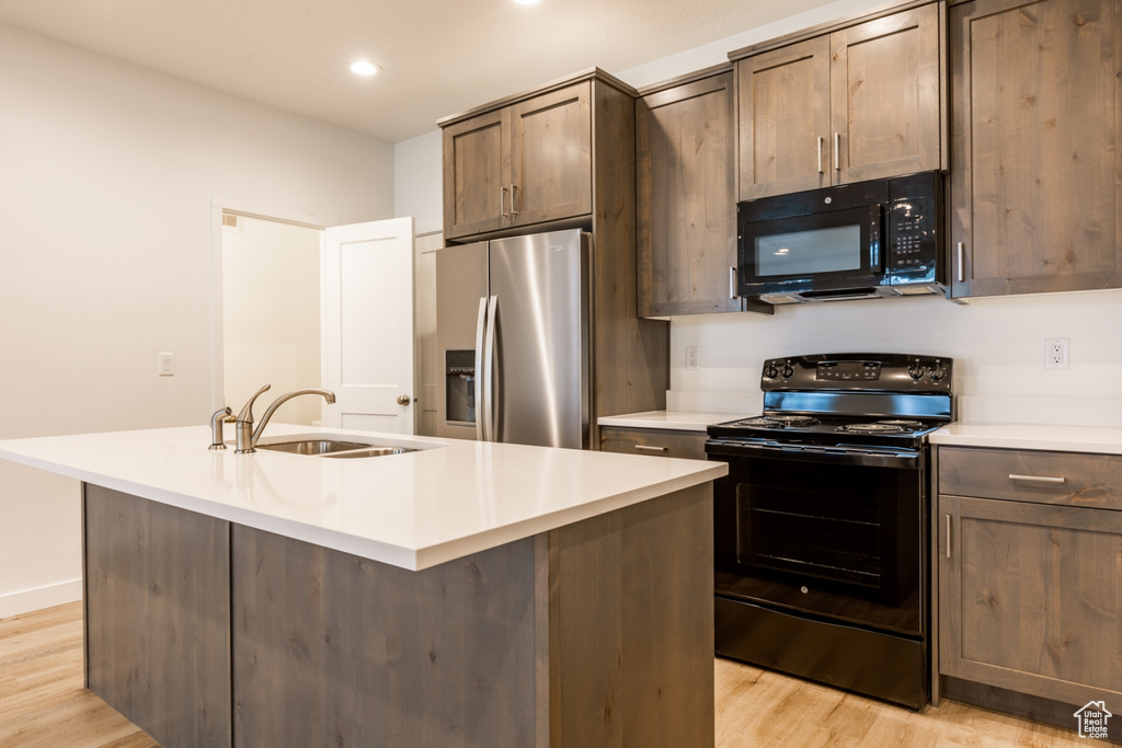 Kitchen featuring sink, black appliances, light hardwood / wood-style floors, and a center island with sink