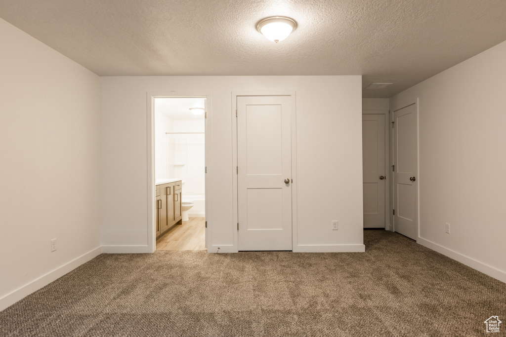 Unfurnished bedroom featuring ensuite bath, light colored carpet, and a textured ceiling