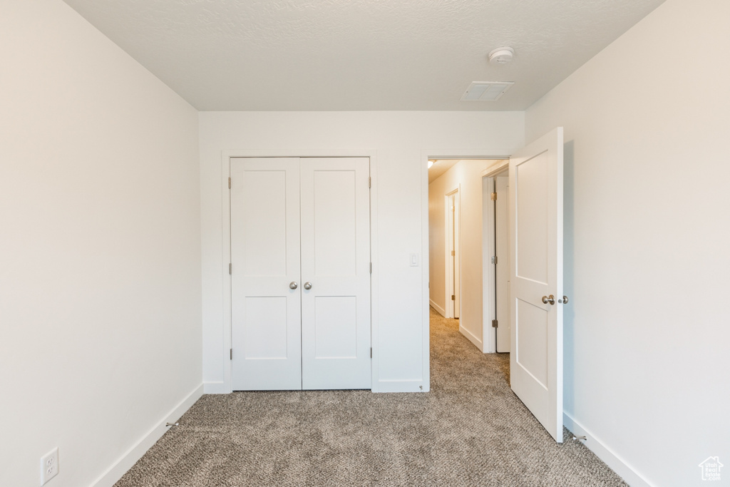 Unfurnished bedroom with light colored carpet, a textured ceiling, and a closet