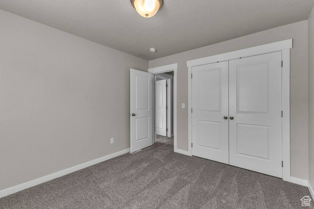 Unfurnished bedroom featuring dark carpet, baseboards, and a closet