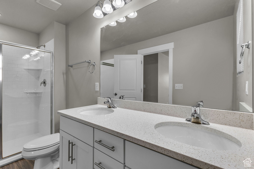 Full bath with toilet, a stall shower, double vanity, and wood finished floors