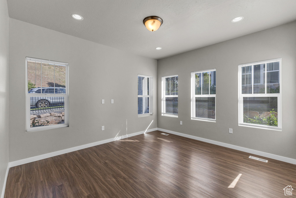 Unfurnished room featuring dark wood finished floors, healthy amount of natural light, baseboards, and recessed lighting