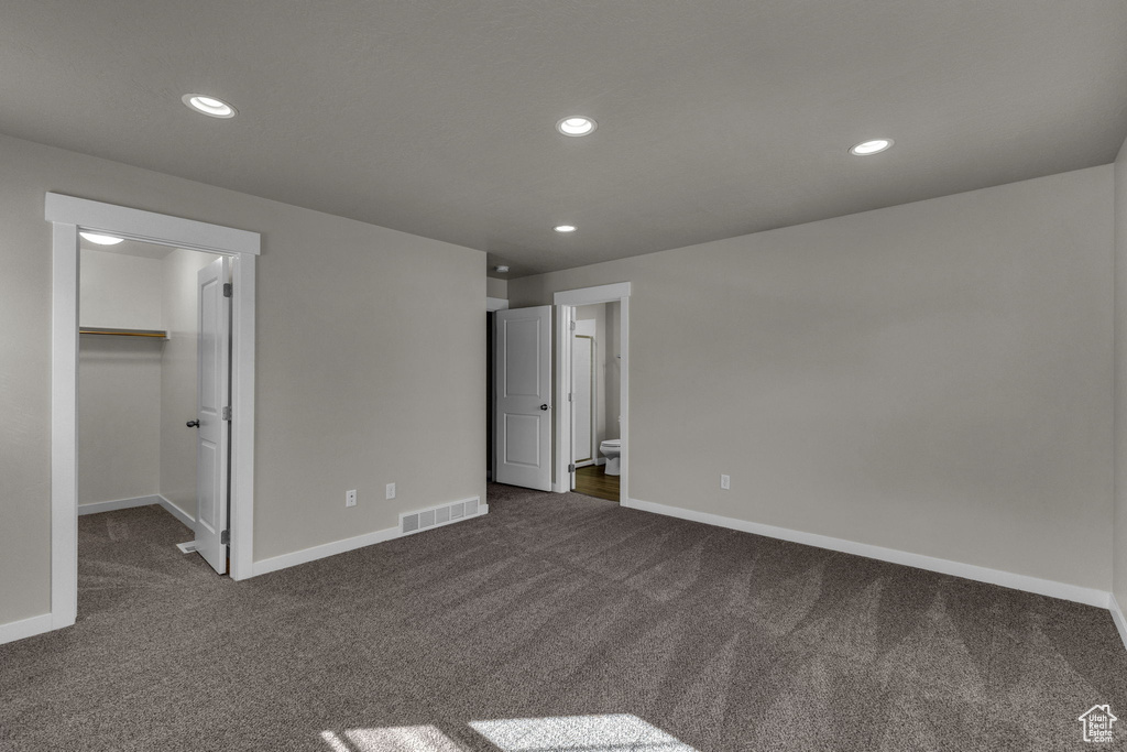 Unfurnished bedroom featuring dark carpet, baseboards, a walk in closet, recessed lighting, and connected bathroom