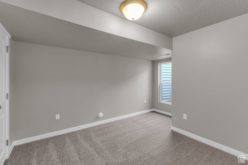 Empty room with carpet flooring, baseboards, and a textured ceiling