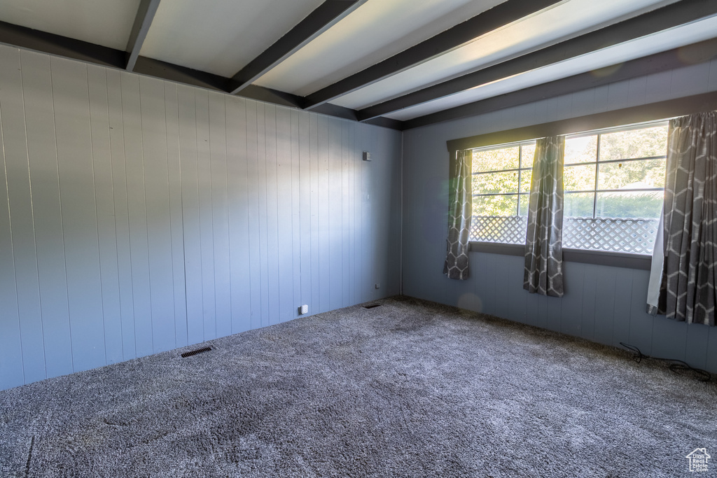 Carpeted spare room featuring beamed ceiling and wood walls