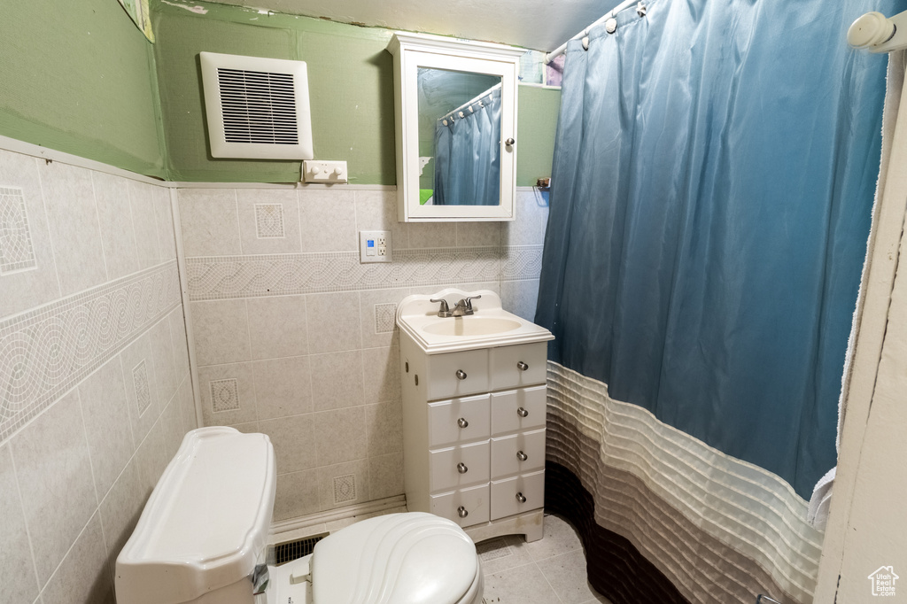 Bathroom featuring toilet, vanity, tile walls, tile patterned flooring, and a shower with shower curtain