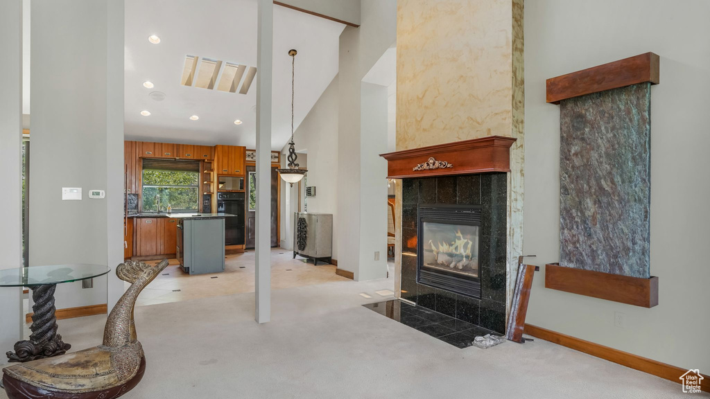 Living room with light colored carpet, a high ceiling, baseboards, a tiled fireplace, and recessed lighting