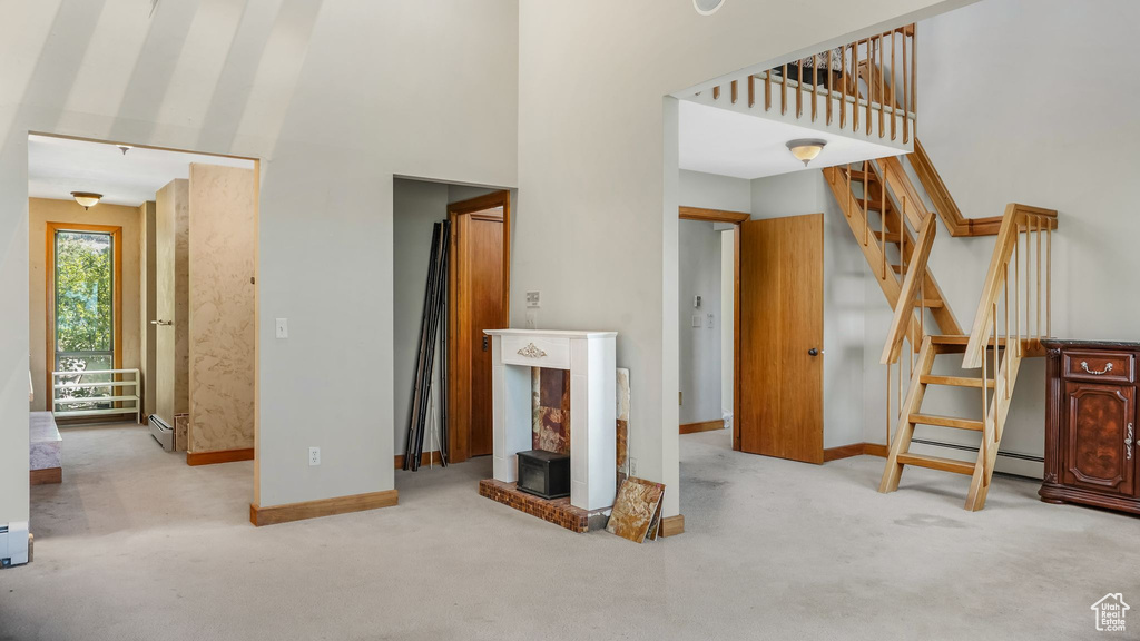 Unfurnished living room with a towering ceiling, carpet flooring, baseboards, and a baseboard heating unit