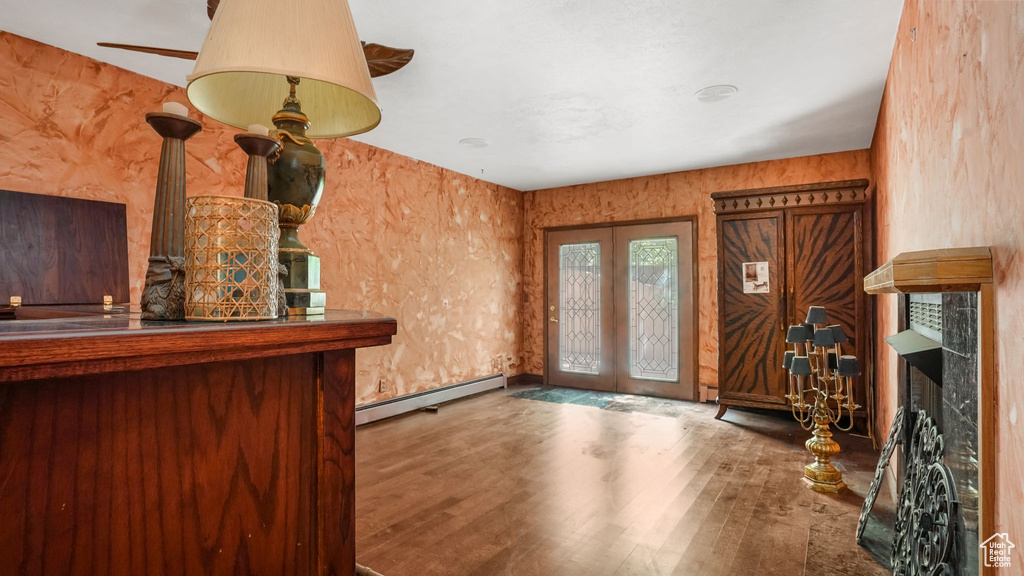 Unfurnished living room with a baseboard radiator, wood finished floors, french doors, and a fireplace
