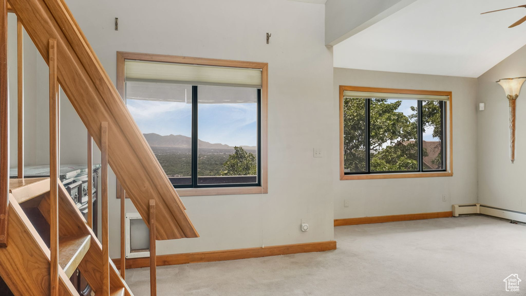 Carpeted empty room featuring healthy amount of natural light, baseboards, baseboard heating, a ceiling fan, and lofted ceiling