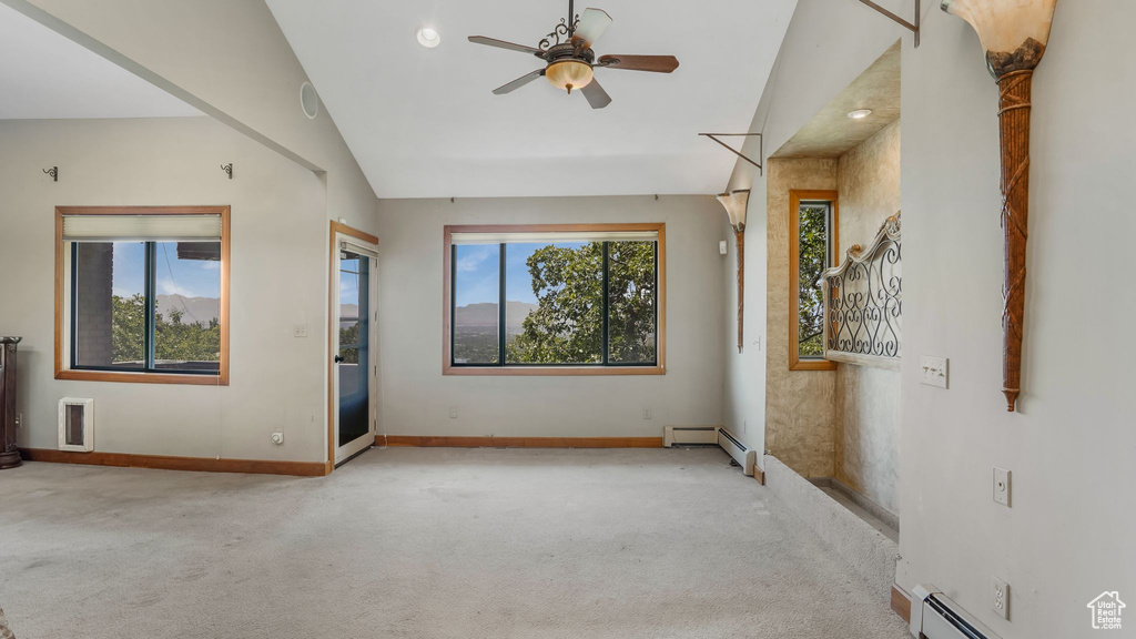 Carpeted spare room featuring vaulted ceiling, ceiling fan, baseboards, and a baseboard radiator
