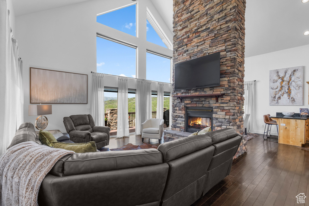 Living area featuring high vaulted ceiling, a stone fireplace, dark wood-style flooring, and baseboards