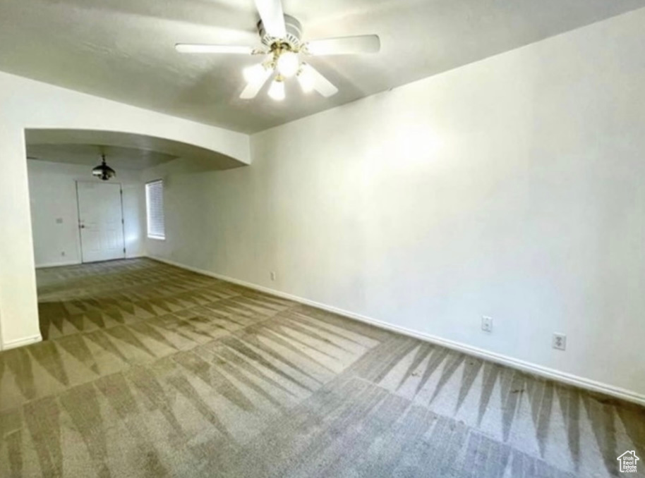 Carpeted spare room with ceiling fan, baseboards, and arched walkways