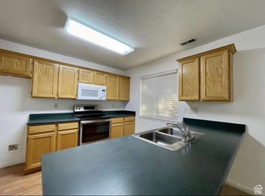 Kitchen with stainless steel range with electric stovetop, white microwave, dark countertops, a sink, and a peninsula
