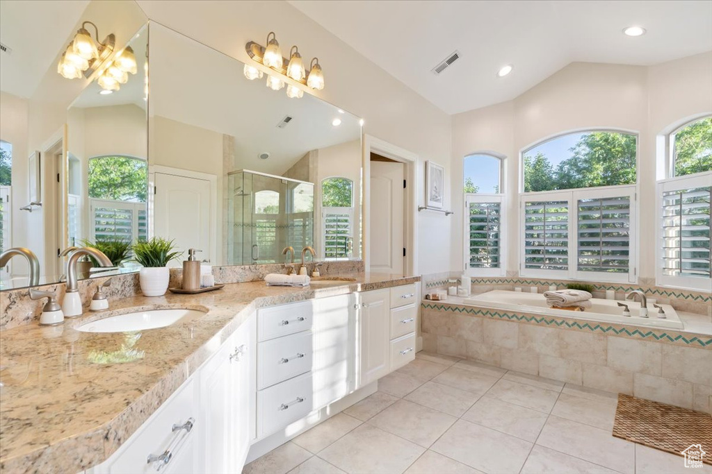 Full bathroom featuring plenty of natural light, lofted ceiling, double vanity, a garden tub, and a stall shower