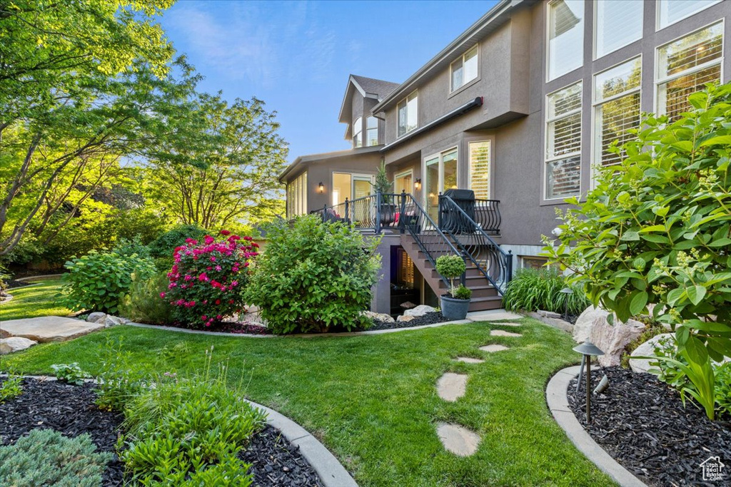 Rear view of property featuring stucco siding, stairs, a lawn, and a wooden deck