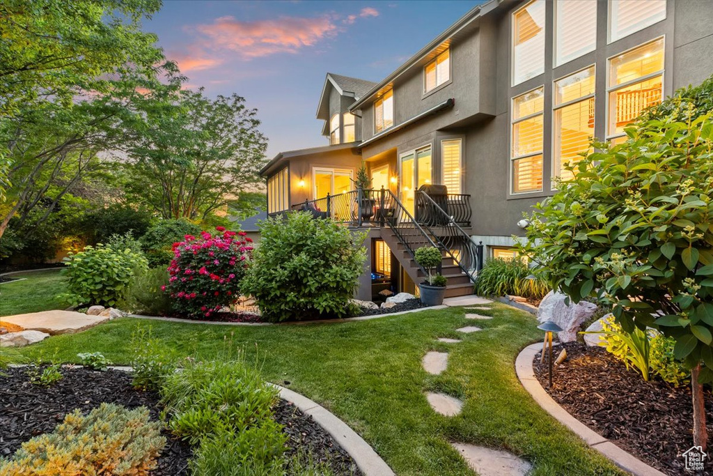 Back of property at dusk with stairs, stucco siding, and a lawn