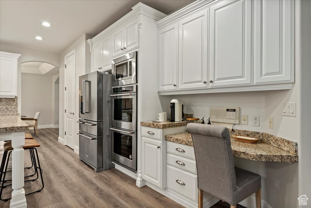 Kitchen with stainless steel appliances, arched walkways, light wood-style flooring, white cabinetry, and recessed lighting
