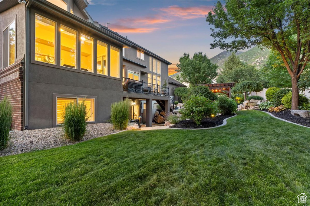 Back of property at dusk with stucco siding, a yard, and a balcony