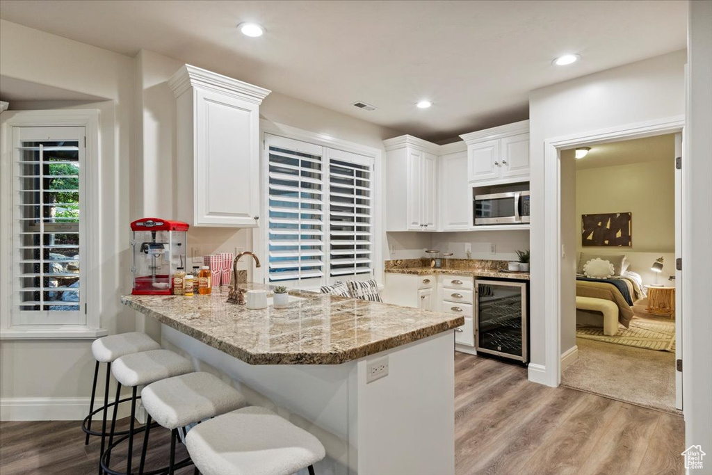Kitchen with beverage cooler, stainless steel microwave, white cabinets, light wood finished floors, and recessed lighting