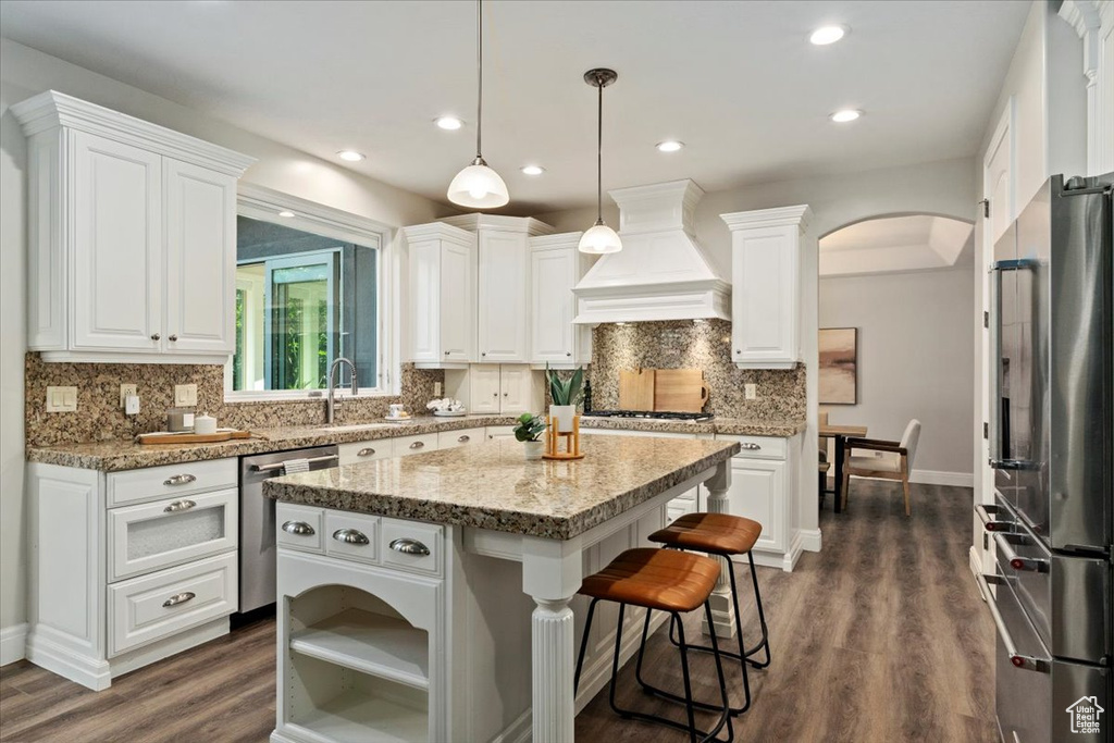Kitchen with stainless steel appliances, custom exhaust hood, white cabinetry, a kitchen island, and dark wood-style flooring