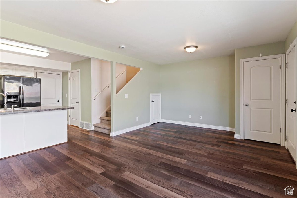 Unfurnished living room with baseboards, stairs, dark wood-type flooring, and a sink