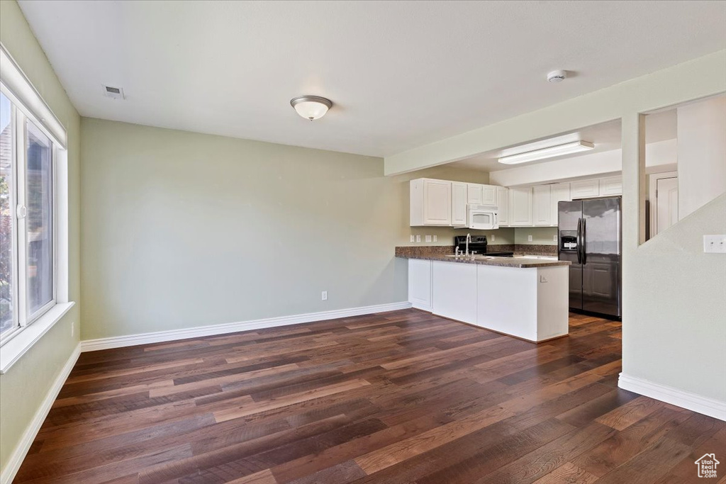 Kitchen featuring stainless steel refrigerator with ice dispenser, white microwave, dark countertops, a peninsula, and black range with electric cooktop