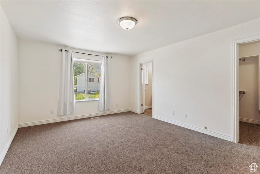 Unfurnished bedroom with a spacious closet, carpet, and baseboards