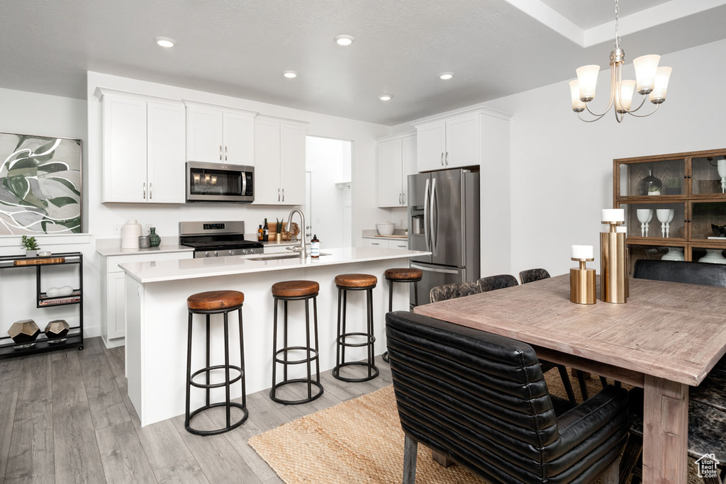 Kitchen with appliances with stainless steel finishes, a sink, a breakfast bar, light wood finished floors, and a chandelier
