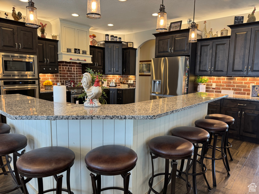 Kitchen featuring appliances with stainless steel finishes, backsplash, a breakfast bar area, a spacious island, and dark wood-style flooring